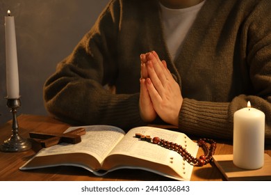 Woman praying at table with burning candles and Bible, closeup - Powered by Shutterstock