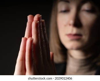 A woman prays. Prayer-clasped hands on a background of a blurred girl face. The girl turns to God. A religious woman. Religion and faith. A young woman's prayer.