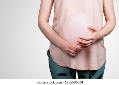 Woman Pregnant Or Bloated Belly. Pink Balloon In Woman's Hands. Abstract Background.