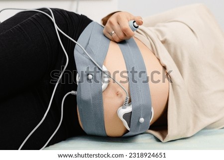 Woman pregnant checking fetal heart beat by fetal monitoring. Expectant mother with midwife adjusting sensors off cardiotocography(CTG).