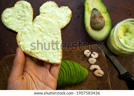 A woman prepares a breakfast of gluten-free bread with shrimp and guacamole. Sandwich in the shape of a heart in a female hand. Valentine's day breakfast.