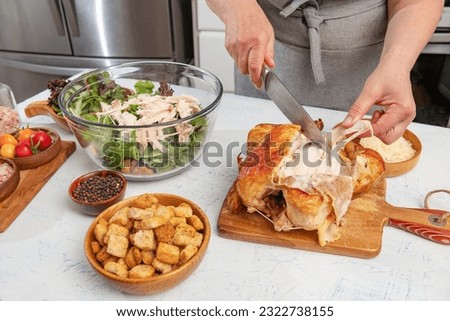 woman prepares a caesar salad in the kitchen. Pieces of fried chicken are added to the salad bowl. Knife and hands close-up.