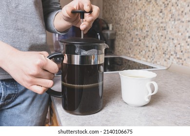 Woman prepares coffee in a French press in her kitchen. Preparing ground coffee in a press. Refreshing drink for breakfast. - Powered by Shutterstock