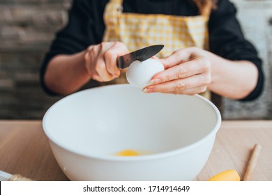 A woman prepares a dough for baking - breaks an egg in a bowl - home cooking - Powered by Shutterstock
