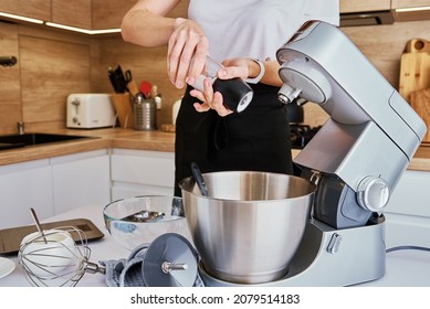 Woman Prepares Dough Using Kitchen Mixer, Pouring Ingredients Into Steel Bowl. Cooking Homemade Cake. Modern Kitchen Appliances