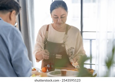 A woman prepares fresh vegetables in a cozy kitchen, while a man assists in the background. The scene emphasizes a warm and healthy lifestyle with a focus on fresh produce and home cooking. - Powered by Shutterstock