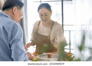 A woman prepares fresh vegetables in a cozy kitchen, while a man assists in the background. The scene emphasizes a warm and healthy lifestyle with a focus on fresh produce and home cooking. - Powered by Shutterstock