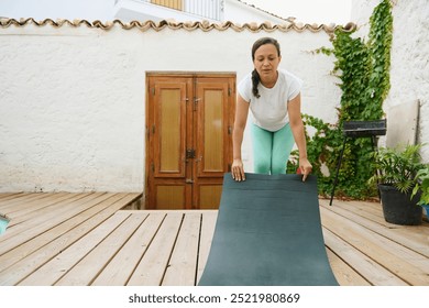 A woman prepares her yoga mat in a tranquil garden setting, ready for outdoor yoga practice surrounded by greenery and a wooden deck. - Powered by Shutterstock