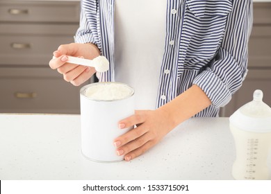 Woman Preparing Baby Milk Formula At Table In Kitchen
