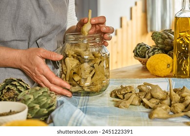 Woman preparing canned italian artichokes in olive oil. Artichoke hearts pickled with olive oil and herbs. Homemade healthy eating.