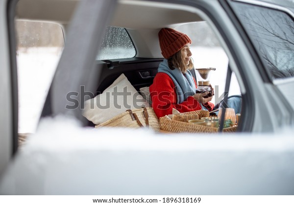 Woman preparing coffee using chemex pour over\
coffee maker in car trunk, traveling by car during winter holidays.\
High quality photo