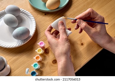 Woman preparing colored easter eggs and painting eggcup for Easter holiday celebration.