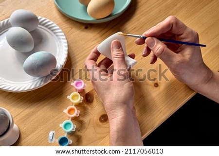 Woman preparing colored easter eggs and painting eggcup for Easter holiday celebration.