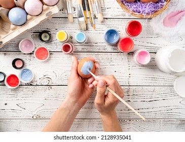Woman preparing for Easter. Home decoration for holiday. Female hands coloring easter eggs with pastel paints, top view flat lay
