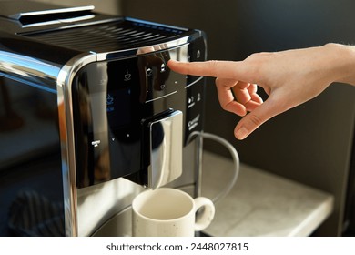 Woman preparing fresh cup of coffee with modern espresso machine. Female hand pressing button on coffee machine