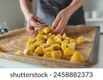 Woman preparing fresh, raw and chopped potatoes on a baking sheet for making roasted potatoes