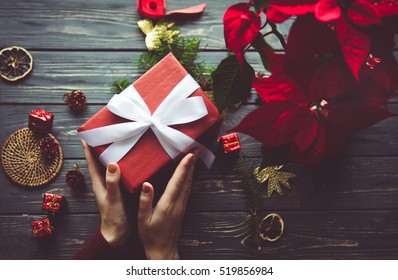Woman preparing gift box for present on table with Poinsettia. Evening before Christmas