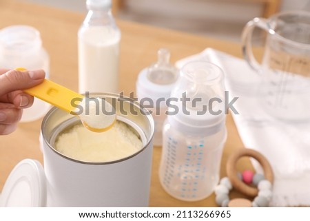 Woman preparing infant formula at table indoors, closeup. Baby milk