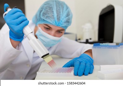 Woman preparing pink samples from pipette for analysing on high quality equipment, blurred background
