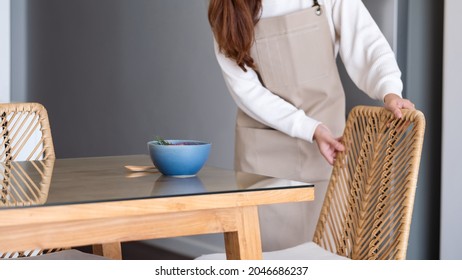 A woman  preparing and setting dining table and chair at home - Powered by Shutterstock