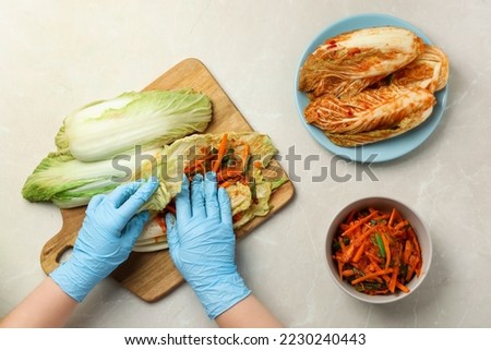 Woman preparing spicy cabbage kimchi at beige marble table, top view