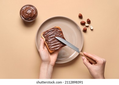 Woman preparing tasty toast with chocolate paste and hazelnuts on beige background - Shutterstock ID 2112898391