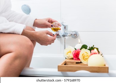 Woman Preparing Wellness Bath With Flowers, Candles And Fragrance Oil In Tub