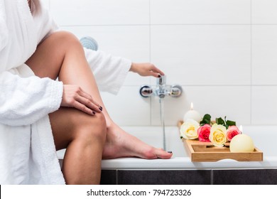 Woman Preparing Wellness Bath With Flowers, Candles And Fragrance Oil In Tub