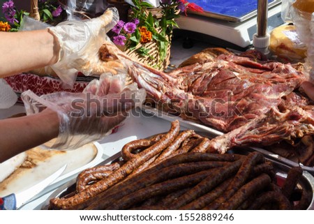 Woman presenting meat specialties during farmer market or food festival. Sausages, bacon, meat produce variety. Raw and cooked. Butchery or shop concept.
