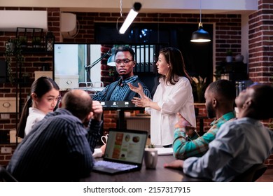 Woman Presenting In Meeting Talking With Business Owner In Video Call Conference In Front Of Team Working Overtime In Startup Office. Startup Coworkers Discussing Sales From Charts On Laptop Screen.