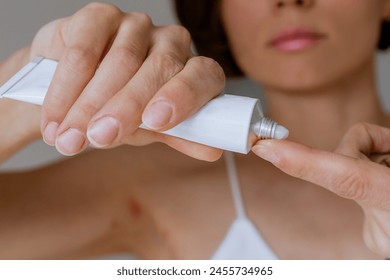 A woman presses the ointment onto her finger and applies it to the bite site by a bedbug on her shoulder on a white background, close-up. Skin health problem. Red pimples. - Powered by Shutterstock