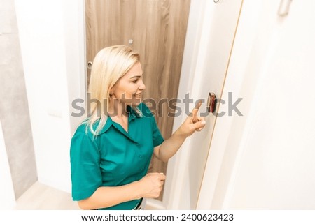 A woman is pressing the up button of a wall attached house thermostat with digital display showing the temperature. A concept image for electricity bill, heating, cooling, eco friendly, saving etc