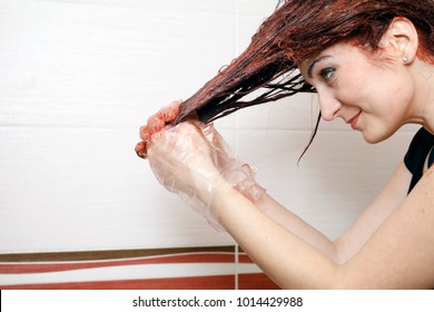 Woman In Process Of Hair Coloring At Home. Applying Red Color To The Hair.