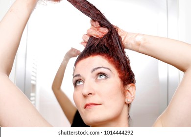 Woman In Process Of Hair Coloring At Home. Applying Red Color To The Hair And Looking Up.