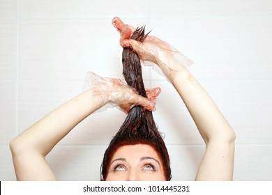 Woman In Process Of Hair Coloring At Home. Applying Red Color To The Hair And Looking Up. 