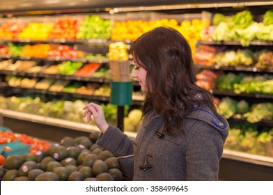 Woman In The Produce Section Of A Supermarket Choosing An Avocado. 