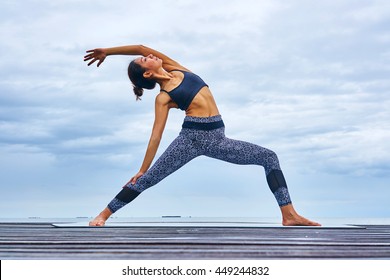 A woman professional trainer yoga pose on wooden bridge over seaside. - Powered by Shutterstock