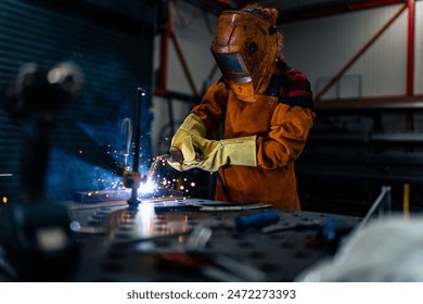 A woman in protective equipment uses tools and machines in the workshop, sparks fly and illuminate the workshop - Powered by Shutterstock