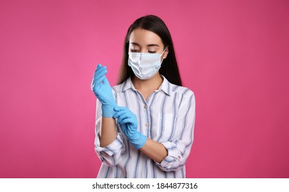 Woman in protective face mask putting on medical gloves against pink background - Shutterstock ID 1844877316