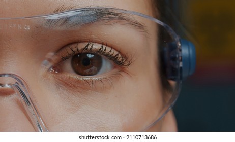 Woman with protective glasses showing one eye in front of camera, brown eye blinking and focusing sight. Person wearing safety goggles, with half of face. Genetic anatomy. Close up - Shutterstock ID 2110713686