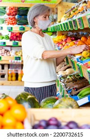 Woman In Protective Mask Choosing Sweet Tangerines And Other Fruit On Counter Of Farmers Market