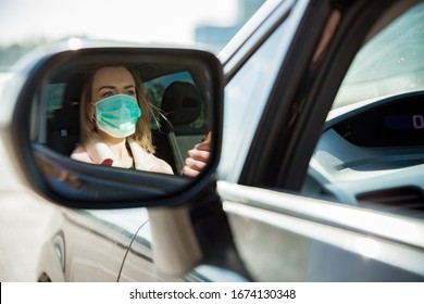 Woman In Protective Mask Driving A Car On Road. Rear-view Mirror Reflection. Safe Traveling.