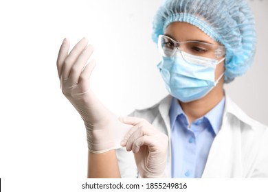 Woman In Protective Mask And Glasses Putting On Medical Glove Against White Background