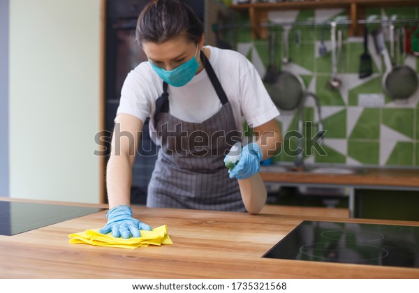 Woman in protective mask and\
gloves cleaning kitchen before start cooking, take away\
kitchen