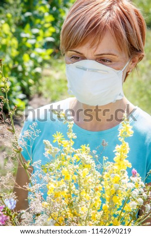 Woman in protective mask holding bouquet of wildflowers and trying to fight allergies to pollen. Natural background. Allergy concept.