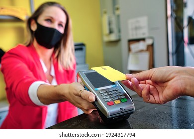 woman with protective mask using credit card to pay contactless