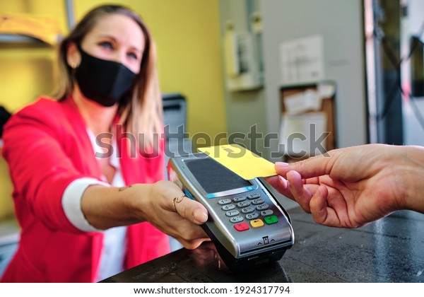 woman with protective mask using credit card\
to pay contactless