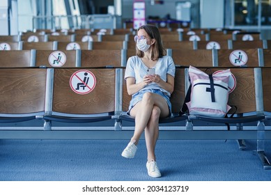 Woman In Protective Mask Waiting For The Plane At The Airport. Beautiful Girl Uses Mobile Phone At Waiting Area In Airport Terminal.