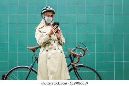 Woman In Protective Maskin, In Helmet Using Her Smartphone Device. Female Go To Work On His Sport Retro Bike. Girl Standing On Green Background.