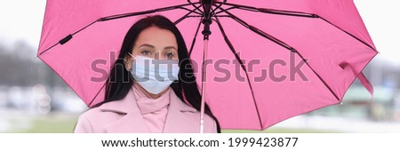 Woman in protective medical mask standing under umbrella